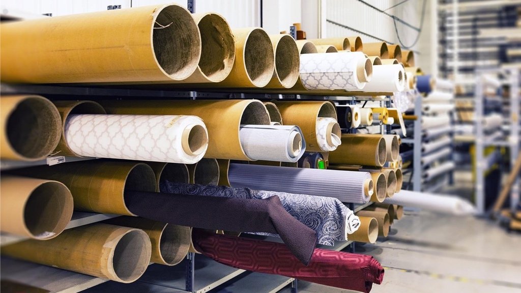 Buscar telas sostenibles y elegir el método de producción adecuado Diseñador de moda revisando rollos de tela y opciones de fabricación